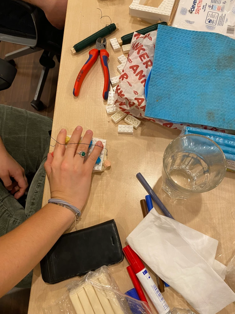 Eine Hand liegt unter einem Drahtbügel auf Maisstärke-Teilen statt Tasten auf einem Gehäuse aus Klemmbausteinen auf Knetmasse auf einem Tisch.
